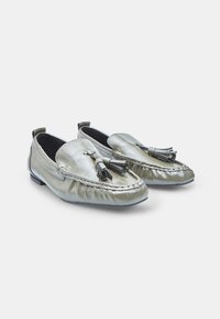 Une paire de mocassins à pampilles gris brillant avec des détails cousus et des orteils légèrement arrondis sur un fond blanc.