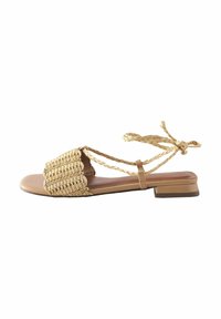 Tan sandalen met een geweven stro bovenkant, vlakke zool en gevlochten enkelbandjes. Vierkante neusontwerp met een textuurpatroon. Lage blokhak.