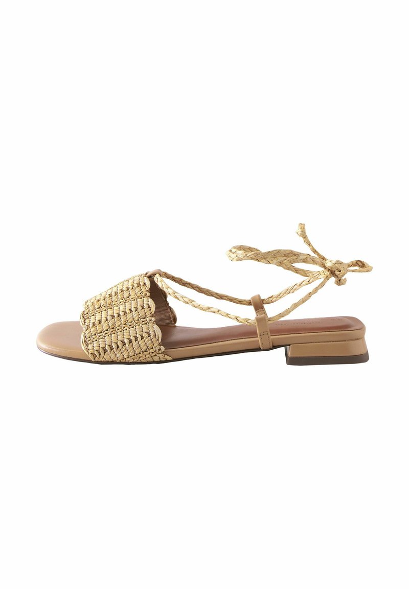 Tan sandalen met een geweven stro bovenkant, vlakke zool en gevlochten enkelbandjes. Vierkante neusontwerp met een textuurpatroon. Lage blokhak.
