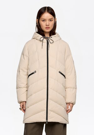 Beżowy puchowy płaszcz z kapturem, z wzorem w jodełkę, czarnymi zamkami błyskawicznymi i ściągaczem; zaprojektowany z przednimi kieszeniami i długą sylwetką.