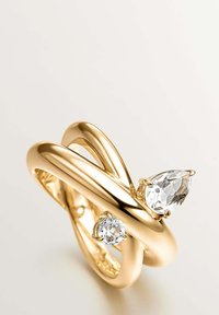 Anillo de oro con un diseño moderno y retorcido que presenta una piedra preciosa en forma de pera y una redonda, ambas transparentes, engastadas en la parte superior.