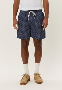 Costum de baie bleu marin cu un model circular, av�ând talie elastică și șnur de ajustare. Purtați cu pantofi bej și șosete albe.