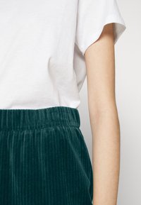 Witte katoenen t-shirt met opgerolde mouwen, gecombineerd met donkerblauwe ribcord broek met elastische tailleband. Textuurdetails zijn zichtbaar.