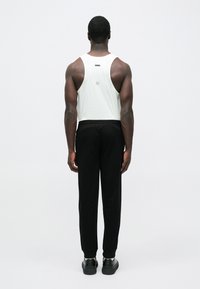 Λευκό αμάνικο αθλητικό τοπ με λογότυπο στην πλάτη, σε συνδυασμό με μαύρο στενό φαρδύ παντελόνι φόρμας. Λείο ύφασμα, εφαρμοστή σχεδίαση και ελάχιστες λεπτομέρειες.