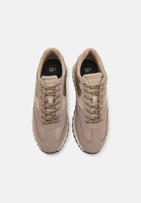 Paire de baskets de sport beige avec dessus en mesh et cuir, lacets beiges, et semelles intérieures noires avec un petit logo, vue de dessus sur fond blanc.