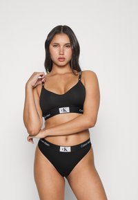 Set di reggiseno e perizoma in cotone nero con logo Calvin Klein sulle bande elastiche. Il reggiseno presenta un design fluido e curvo con spalline sottili.