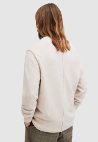 Helles beige gestricktes Sweatshirt aus weichem Material, mit Rundhalsausschnitt und gerippten Bündchen, und einer Nahtdetails auf der Rückseite.