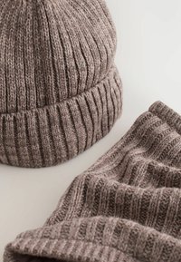 Braunes gestricktes Mütze- und Schal-Set mit gerippter Textur, weichem Garn und umgeschlagenem Bündchen an der Mütze, auf einem hellen Hintergrund präsentiert.