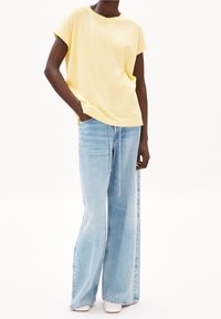Yellow short-sleeve t-shirt with rolled cuffs, paired with light blue wide-leg jeans featuring a drawstring and distressed details.