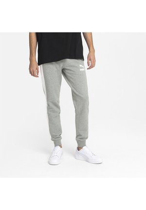 Pantalones de chándal grises con puños y rayas laterales blancas, y logo de Puma en el muslo, combinados con zapatillas blancas y una camiseta negra.
