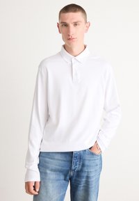 Hvit langermet polo skjorte med klassisk krage og treknapplukking, kombinert med lyseblå denimjeans. Glatt tekstur, avslappet passform.