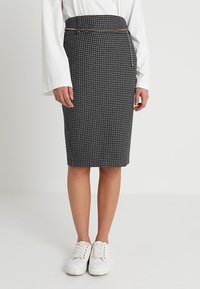 Černobílá sukně s houndstooth vzorem, tužkového střihu, s vysokým pasem a opaskem se zlatými akcenty, doplněná bílými teniskami. Hladká textura.
