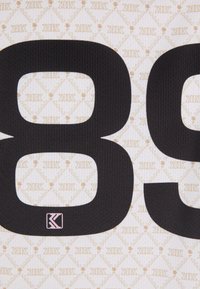 Černá tkanina s výraznými čísly "8" a "9" na světlém, vzorovaném pozadí s béžovými motivy a jemnou texturou, a s malým logem.