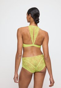 Bralette en dentelle et briefs assortis en vert néon vif avec des motifs floraux, présentant une conception à col haut et un dos ouvert.