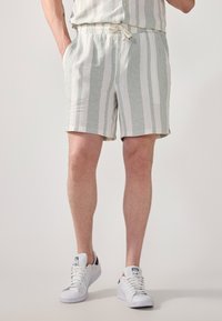 Shorts rayés en vert clair et blanc, fabriqués en tissu texturé. Dotés d'une taille élastique avec cordon de serrage et de poches latérales.