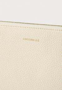 Coccinelle pénztárca texturált krémszínű bőrből, arany cipzárral és dombornyomott logóval. Simább felülettel és finom szemcse részletekkel rendelkezik.
