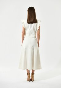 Vit midiklänning med volangärmar, åtsittande liv och utsvängd kjol. Mjuk tyg med subtil textur. Ett par beige klacksandaler.