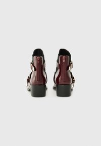 Bottines bordeaux en cuir verni avec une finition lisse, dotées d'une fermeture éclair sur le côté et d'un talon block. Panneaux élastiques noirs sur les côtés.