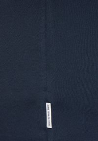 Marineblauer, dehnbarer Stoff mit glatter Textur, der an der Seite mit einem kleinen weißen Etikett versehen ist, auf dem "Marc O'Polo DENIM" steht.