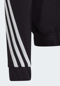 Manica di giacca sportiva nera con design a tre strisce bianche. Presenta un polsino a costine e una texture liscia. Vita elastica per una vestibilità comoda.