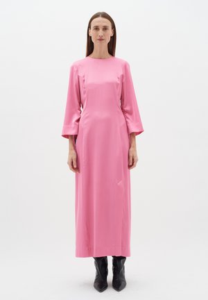 Lang pink satin kjole med lange ærmer, en lige silhuet og sidelommer. Båret med sorte spidse støvler.
