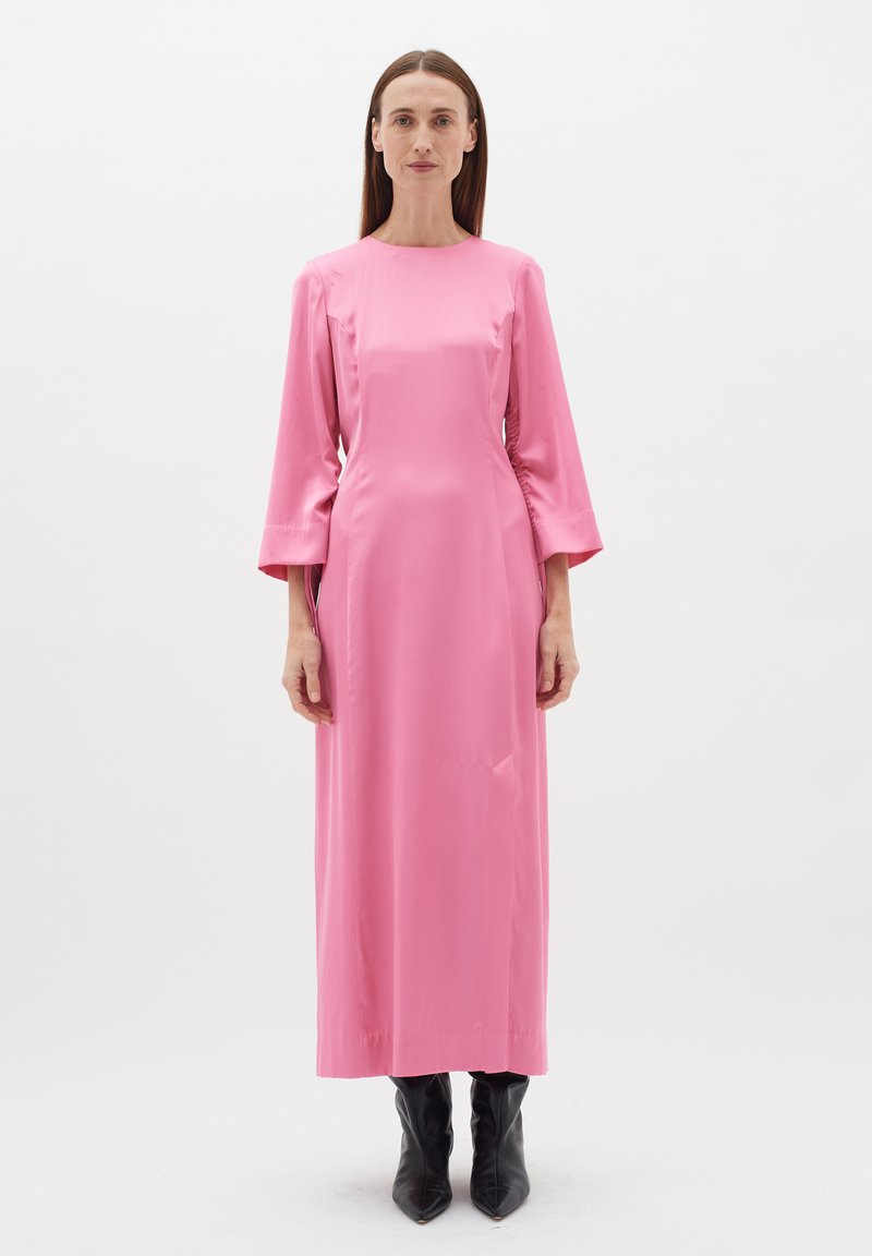 Rochie lungă din satin roz, cu mâneci lungi, siluetă dreaptă și buzunare pe laturile cusăturii. Purtați-o cu cizme negre cu vârful ascuțit.
