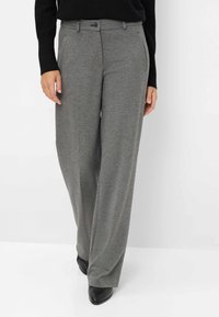 Pantaloni grigi a gamba larga realizzati in tessuto morbido, dotati di chiusura con bottone, passanti per cintura e tasche laterali, abbinati a scarpe nere.