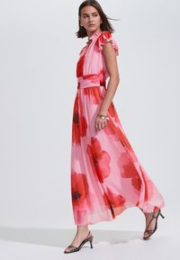 Áttetsző rózsaszín anyagból készült maxi ruha nagy piros virágmintákkal, fodros ujjakkal és testhezálló derékrésszel. Strapabíró, magas sarkú szandálokkal párosítva.