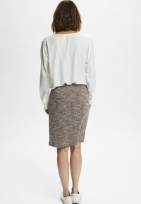 White long-sleeve blouse with pleated shoulders, paired with a multicolored tweed pencil skirt and casual white shoes.