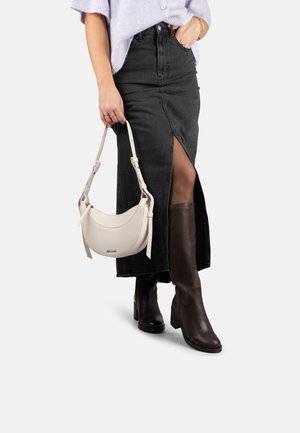 Sac à main en cuir blanc avec une bandoulière ajustable, associé à une jupe en denim noire avec une fente devant, et des bottes en cuir marron jusqu'au genou.