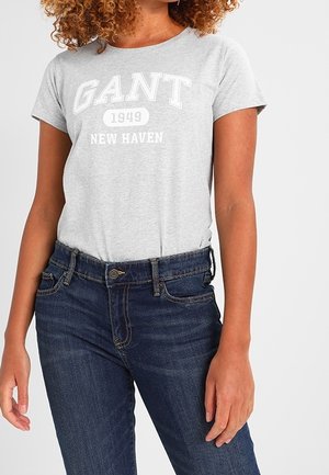 Grå T-shirt med korte ærmer, der har "GANT 1949 NEW HAVEN" i hvid skrift, parret med mørke denim jeans med klassisk pasform.
