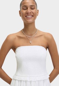 Top bianco senza spalline con texture arricciata, orlo a volant e collane a strati di perline, con dettagli in argento e perle.
