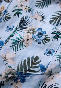 Korte mouwen shirt van lichtblauwe stof met een bloemenpatroon van blauwe en crèmekleurige bloemen en groene bladeren, inclusief een borstzak.