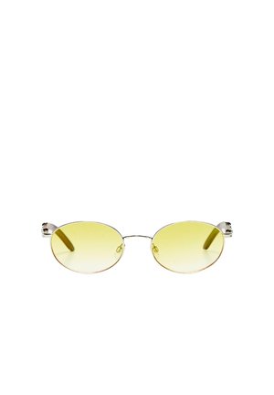 Lunettes de soleil ovales teintées jaune avec fines montures en métal argenté et plaquettes de nez sur fond blanc.
