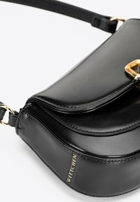 Czarna skórzana torebka o zaokrąglonym kształcie, z złotym akcentem hardware i wytłoczonym logo. Gładka faktura z przeszyciami.