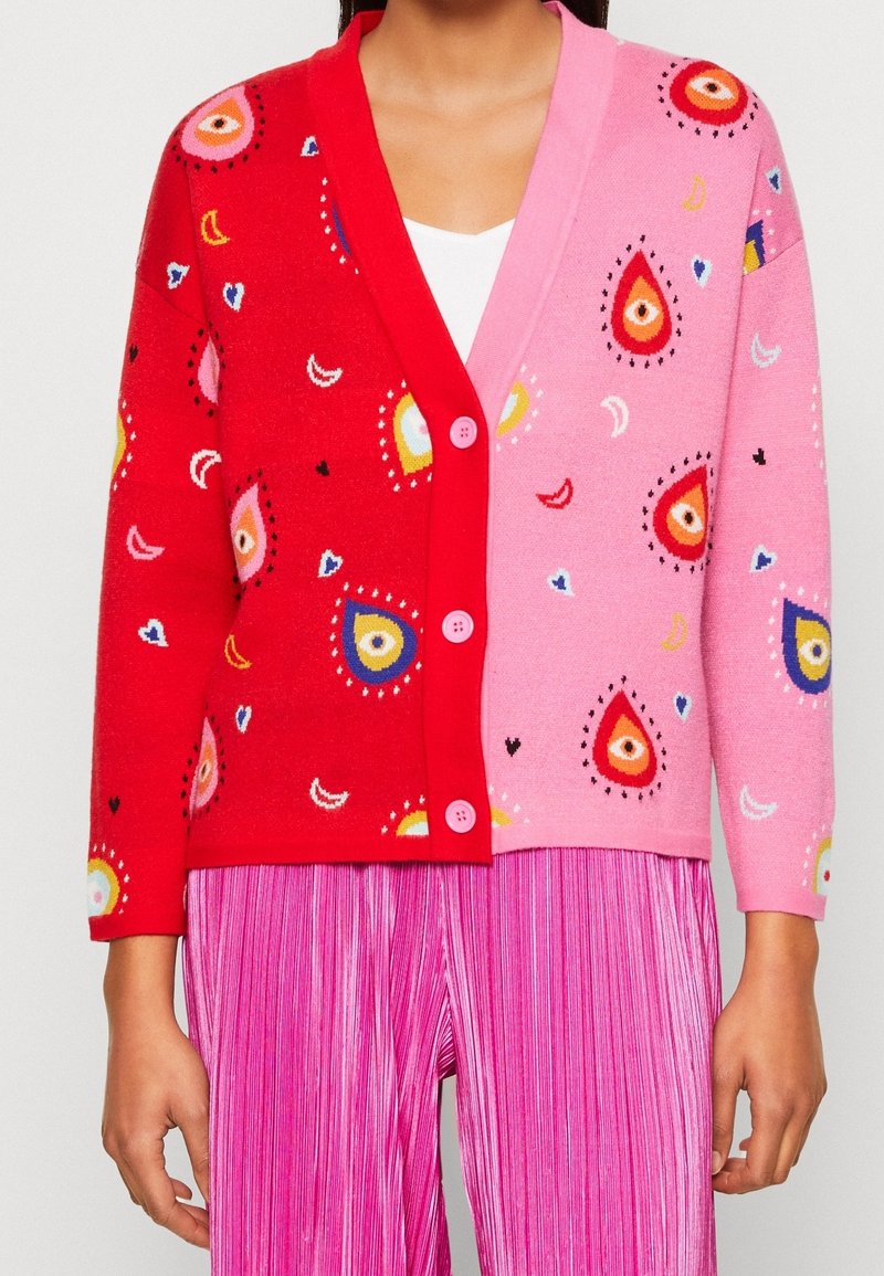 Cardigan coloré avec tissu rouge et rose orné de motifs en forme de gouttes, boutons décoratifs, et coupe décontractée. Matière tricotée texturée.
