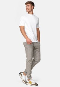 T-shirt bianco in cotone, pantaloni elasticizzati grigio chiaro e sneakers da ginnastica multicolori con accenti gialli. Tessuto liscio, vestibilità casual.