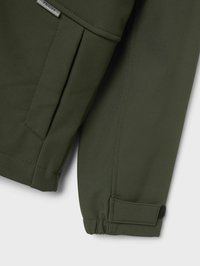 La manche de la veste technique verte montre un tissu lisse, un poignet élastique avec Velcro, et une poche avec un pli, mettant en avant sa fonctionnalité.