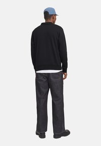 Sort sweatshirt med en afslappet pasform, parret med mørke denimbukser med kontraststing og sorte sko. En lys blå kasket fuldender looket.