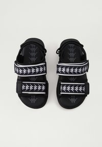 Svarte sandaler med justerbare stropper som har et svart-hvitt mønster. Tykk gummisåle gir støtte. Teksturert såle for bedre grep.