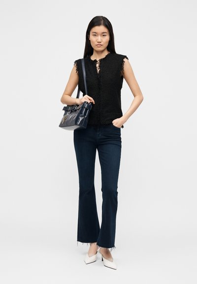 Top preto sem mangas com textura e bordas desfiadas, combinado com jeans azul-escuro flare e sapatos brancos de salto. Mala escura com detalhe de fivela.