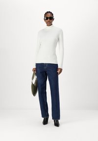 Pull en maille côtelée blanc, jean en denim bleu à jambes droite, bottines à talons noires, et sac à main vert.