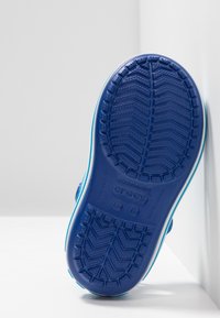 Suela de zapato de goma azul con un patrón de agarre texturizado y un borde azul claro en contraste. Cuenta con agujeros de drenaje y una marca en relieve.