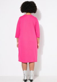 Abito rosa a lunghezza ginocchio realizzato in tessuto morbido, con maniche a tre quarti e scollatura rotonda, abbinato a stivali argento alla caviglia.