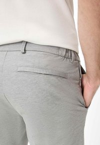 Pantaloni grigi chiari con una texture liscia, vita elastica e una tasca posteriore singola. Tasca laterale visibile; design casual.