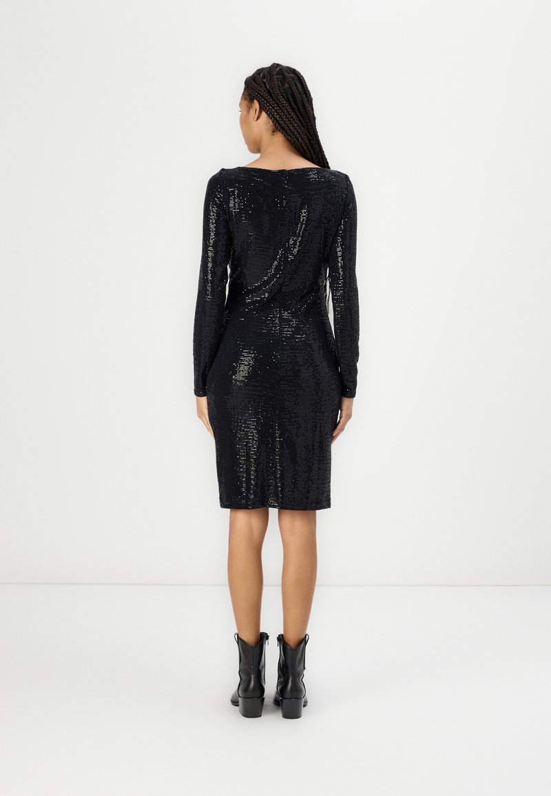 Czarna sukienka z cekinami, z długimi rękawami, dopasowanym krojem, okrągłym dekoltem i długością do kolan. Noszona z czarnymi botkami za kostkę.
