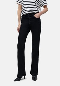 Pantalons évasés noirs à taille haute, dotés d'une fermeture frontale à cinq boutons et d'une texture lisse, associés à une chemise rayée et des talons.