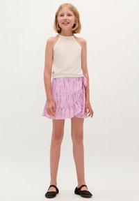 White knit halter top with open back, paired with a pink tie-dye wrap skirt featuring ruffles, worn with black flats.