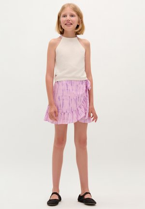 White knit halter top with open back, paired with a pink tie-dye wrap skirt featuring ruffles, worn with black flats.