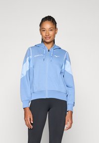 Sweatshirt de zíper azul claro com capuz. Apresenta detalhes em azul escuro nos ombros e mangas, cordões e o logótipo "Mizuno" no peito.